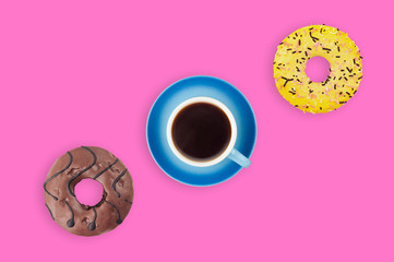 Full blue mug of hot black coffee near different sweet round donuts on pink table. Top view. Working break concept