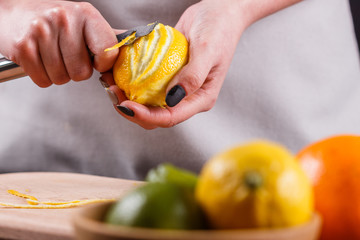 young woman in a gray aprons cuts lemon zest