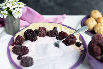 fruity yogurt with banana slices, frozen forest fruits and almond nut flakes on a plate surrounded by frozen berries and sweet buns