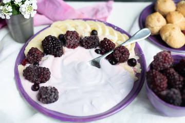 fruity yogurt with banana slices, frozen forest fruits and almond nut flakes on a plate surrounded by frozen berries and sweet buns
