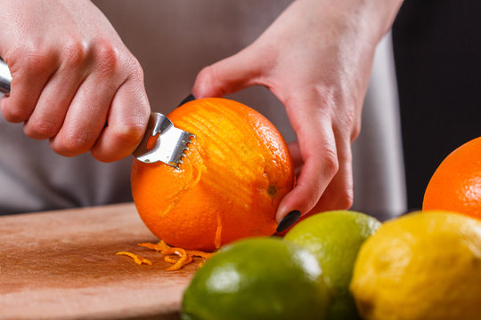 young woman in a gray aprons, cuts an orange zest