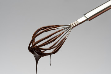 Whisk with liquid melted chocolate on light grey background