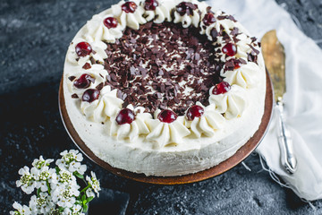German, delicious Black Forest cake, with a delicate white cream, cherries in alcohol and dark chocolate on a dark stone table decorated with white linen fabric