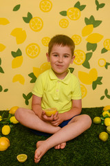 The boy sits and eats lemons and limes, smiles and twists from citrus acid