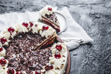 German, delicious Black Forest cake, with a delicate white cream, cherries in alcohol and dark chocolate on a dark stone table decorated with white linen fabric