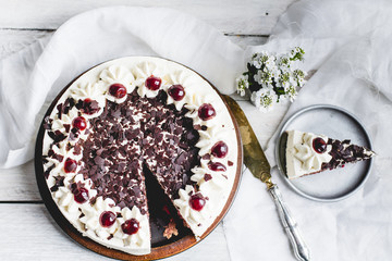 German, delicious Black Forest cake, with a delicate white cream, cherries in alcohol and dark chocolate on a white wooden background decorated with white linen fabric and white flowers