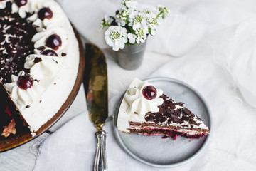 German, delicious Black Forest cake, with a delicate white cream, cherries in alcohol and dark chocolate on a white wooden background decorated with white linen fabric and white flowers