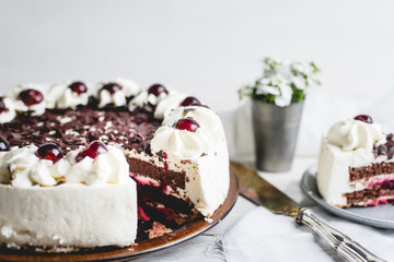 German, delicious Black Forest cake, with a delicate white cream, cherries in alcohol and dark chocolate on a white wooden background decorated with white linen fabric and white flowers