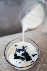 Pouring fresh milk on black grass jelly 