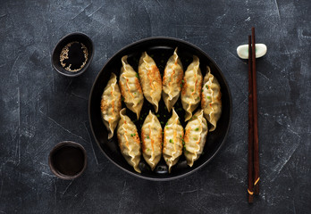 Fried dumplings Gyoza in pan, soy sauce, chopsticks on dark stone background, top view