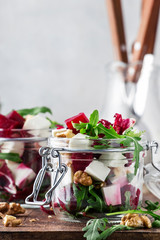 Beet salad with arugula, cheese and walnuts, summer salad jar, gray kitchen table background, copy space, selective focus