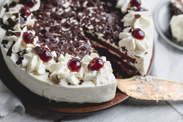 German, delicious Black Forest cake, with a delicate white cream, cherries in alcohol and dark chocolate on a white wooden background decorated with white linen fabric
