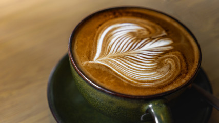 A beautiful dark cappuccino coffee created in a coffee shop in thailand, stoneware mug with a cappuccino with perfect Latte Art Served on a wooden table.