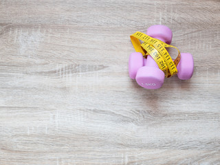 Fitness equipment with dumbbells and measuring tape on wooden floor background. Top view from above. Health and exercise concept with copy space