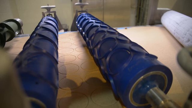 Machine with blue roller in bakery that cuts flat dough into circles.