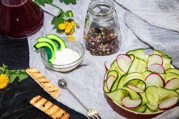Cucumber sliced ​​thin slices, radish thin slices, sauce of sour cream and mayonnaise, green peas, all against a dark background. Spring vegetables