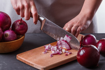young woman in a gray aprons cuts red onion