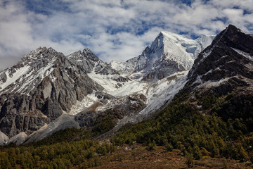 Chenadorje, holy snow mountain in Daocheng Yading Nature Reserve - Garze, Kham Tibetan Pilgrimage region of Sichuan Province China. Clouds blowing off the top of snow capped mountain