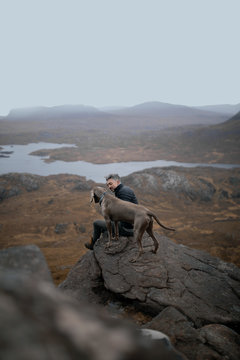 man and a dog on a rock on top of a mountain