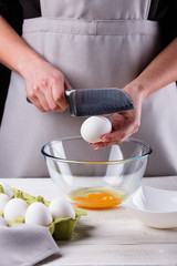 young woman in a gray aprons breaks the eggs