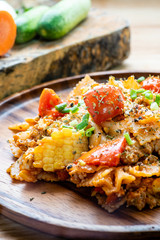 farfalle pasta in tomato sauce with chicken and pork on wooden plate