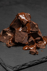 dark or milk chocolate pieces stack and chocolate syrup on dark concrete background