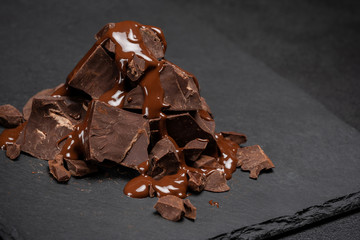 dark or milk chocolate pieces stack and chocolate syrup on dark concrete background