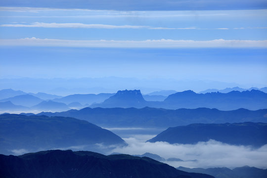 Abstract Image, Mountain Silhouettes at dawn - rolling jagged mountain peaks, cold blue color hues. Panoramic Abstract Background Image, overcast skies, layers of rolling mountains in the distance.