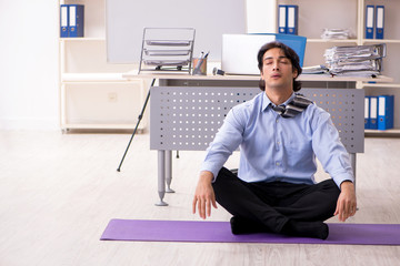 Young handsome male employee doing exercises in the office 