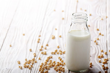 Non-dairy alternative Soy milk or yogurt in glass bottle on white wooden table with soybeans aside
