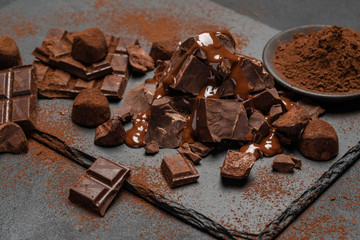 dark or milk chocolate pieces, chocolate syrup and truffle candies on dark concrete background