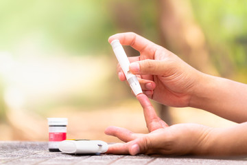 Close up of woman hands using lancet on finger to check blood sugar level by Glucose meter using as...