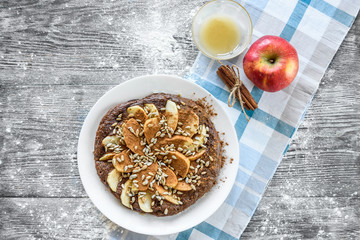 Chocolate oat pancake with apple and sunflower seeds on gray wooden background.