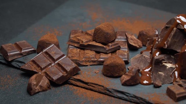 dark or milk chocolate pieces, chocolate syrup and truffle candies on dark concrete background