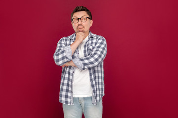 Portrait of thoughtful handsome middle aged business man in casual checkered shirt and eyeglasses standing, looking away and thinking what to do.