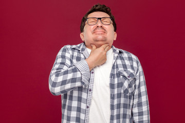 Throat pain on cold. Portrait of middle aged man in casual checkered shirt and eyeglasses standing and holding his painful neck because his sick