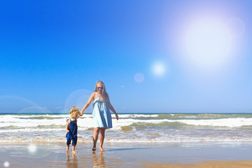 Mom and daughter are walking on the beach. Front view, copy space.