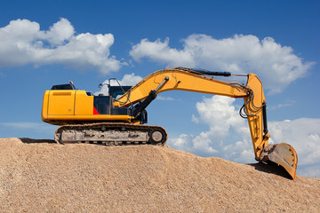 Yellow excavator on a pile of dirt with blue sky with white clouds in the background
