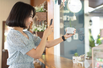 Asian young woman take a photo of cactus pots by smartphone , smiling woman holding mobile devices  in nature background