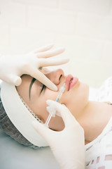 Naklejka premium a girl in a white sterile hat is lying on a couch with a beautician and she is given injections to increase her lips