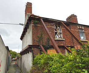 Front walls of derelict house propped up from collapsing by steel poles. 