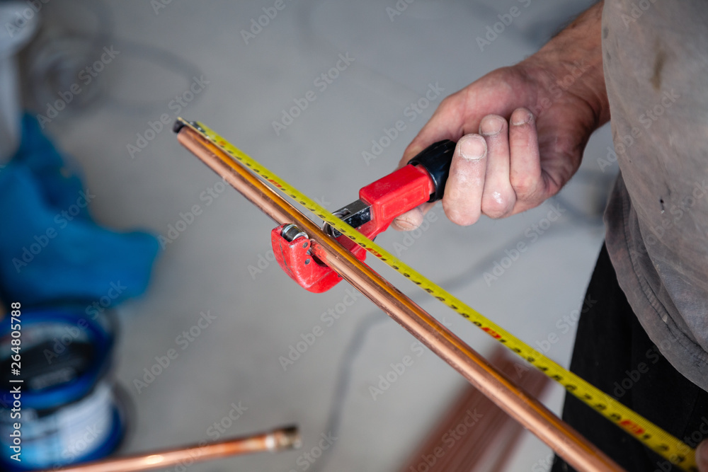 Wall mural Closeup worker plumber master measures copper pipes with roulette tape, cut pipe with cutter. Concept installation, changing pipeline, repair, leakage, breaking sewage