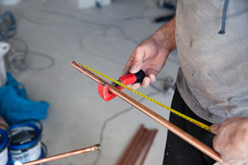 Closeup worker plumber master measures copper pipes with roulette tape, cut pipe with cutter. Concept installation, changing pipeline, repair, leakage, breaking sewage