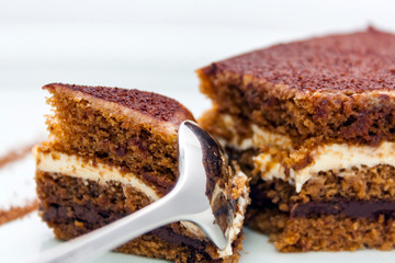 a piece of delicious chocolate cake, which is divided by a shiny spoon; close-up on a white background