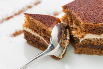 a piece of delicious chocolate cake, which is divided by a shiny spoon; close-up on a white background