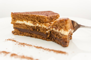 a piece of delicious chocolate cake, which is divided by a shiny spoon; close-up on a white background