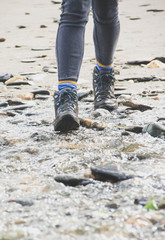 Women's hiking boots crossing river on beach