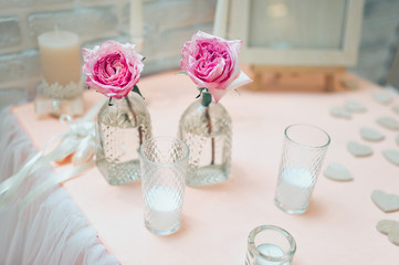 Large pink roses stand in glass vases along with candles in glass cups. Wedding ceremony. Scenery and details. Evening rites and traditions.