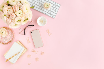 Stylized, pink women's home office desk. Workspace with computer, bouquet ranunculus and roses, phone, clipboard, feminine golden fashion accessories isolated on pink background. Flat lay. Top view.