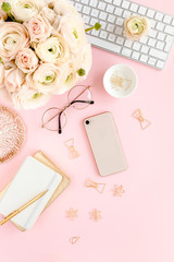 Stylized, pink women's home office desk. Workspace with computer, bouquet ranunculus and roses, phone, clipboard, feminine golden fashion accessories isolated on pink background. Flat lay. Top view.